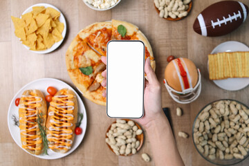 Hand Holds White Blank Screen Smartphone for Sport Match and Food Advertisement Mockup on Wooden...