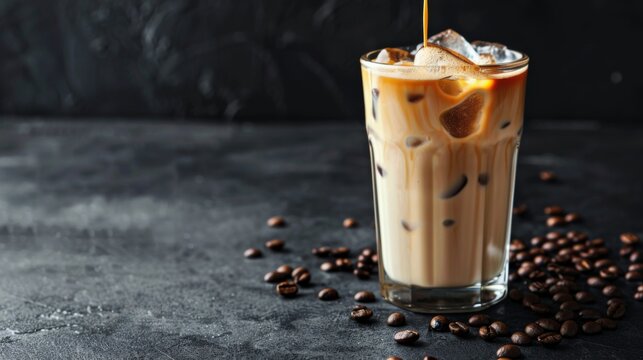 Ice coffee in a tall glass with cream poured over, ice cubes and beans on a dark concrete table. Cold summer drink with tubes