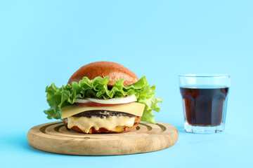 Wooden board with tasty burger and glass of cola on blue background