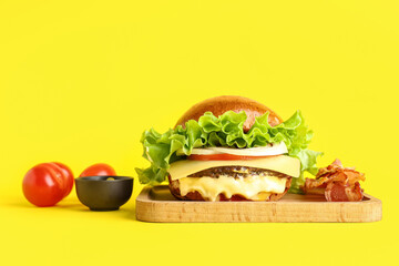 Tasty burger with bacon, sauce and tomatoes on yellow background