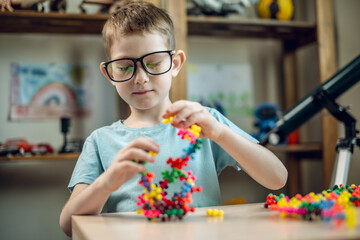 A child boy in the children's room is playing with a toy constructor for teaching the science of chemistry. Assembling molecules from elements. Children's scientific education - 785856682
