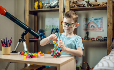 A child boy in the children's room is playing with a toy constructor for teaching the science of chemistry. Assembling molecules from elements. Children's scientific education - 785856814