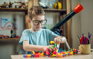 A child boy in the children's room is playing with a toy constructor for teaching the science of chemistry. Assembling molecules from elements. Children's scientific education - 785857269
