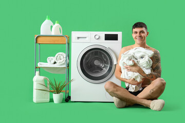 Young man in underpants with laundry and washing machine on green background