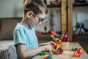 A child boy in the children's room is playing with a toy constructor for teaching the science of chemistry. Assembling molecules from elements. Children's scientific education
