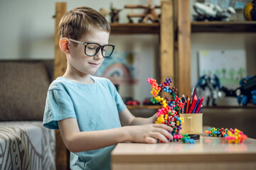 A child boy in the children's room is playing with a toy constructor for teaching the science of chemistry. Assembling molecules from elements. Children's scientific education - 785858291