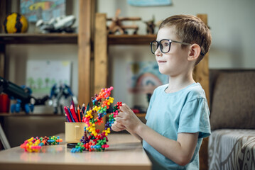 A child boy in the children's room is playing with a toy constructor for teaching the science of chemistry. Assembling molecules from elements. Children's scientific education - 785858413