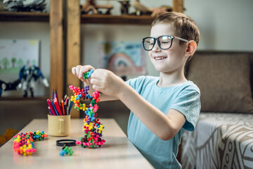 A child boy in the children's room is playing with a toy constructor for teaching the science of chemistry. Assembling molecules from elements. Children's scientific education - 785858486