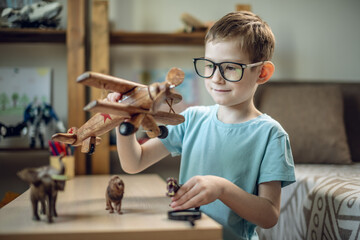 A child boy in the children's room is playing with a toy wooden airplane with animals of the savannah. Fantasies of great adventures and travels - 785858841