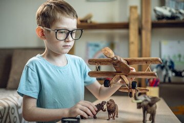 A child boy in the children's room is playing with a toy wooden airplane with animals of the savannah. Fantasies of great adventures and travels - 785859058