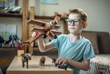 A child boy in the children's room is playing with a toy wooden airplane with animals of the savannah. Fantasies of great adventures and travels - 785859212