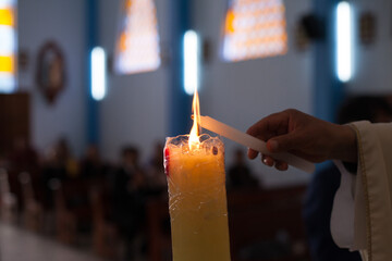 Photograph of unrecognizable hands lighting a candle in a church.