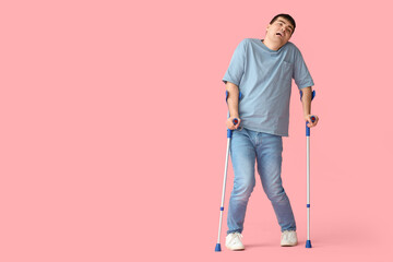 Young man with crutches on pink background. National Cerebral Palsy Awareness Month