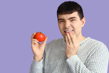 Young man with tomato suffering from toothache on lilac background, closeup