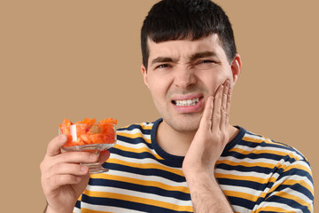 Young man with candies suffering from toothache on brown background, closeup