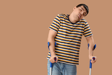 Young man with crutches on brown background. National Cerebral Palsy Awareness Month