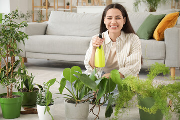 Young woman sitting on floor and spraying houseplants at home