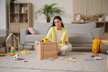 Tired young mother resting among scattered children's toys in living room