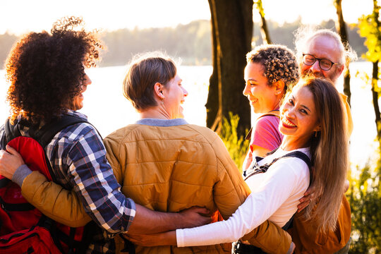 This heartwarming image captures a multigenerational family enjoying a moment of togetherness by a lake at sunset. The group is engaged in a group hug, with joyful expressions and an aura of
