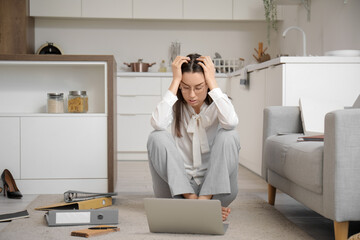 Tired young businesswoman sitting on floor with laptop and office folders at home