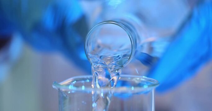 Water is poured from a bottle into a glass beaker in lab