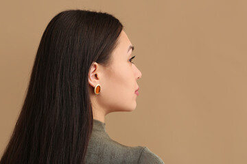Young woman with beautiful earrings on beige background