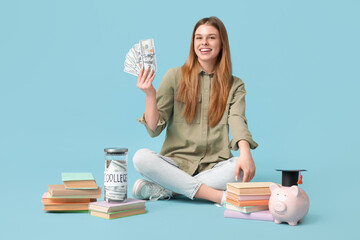 Female student sitting with piggy bank in graduation hat, money and books on blue background....