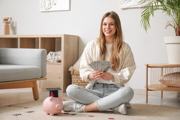 Female student sitting on floor with piggy bank in graduation hat and money in room. Concept of savings for education - obrazy, fototapety, plakaty