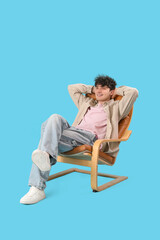 Young man resting in comfortable armchair on blue background