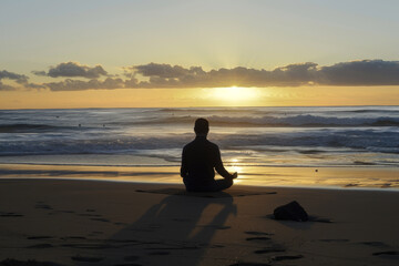 Fototapeta premium A person meditating on the beach at sunrise, their posture serene.