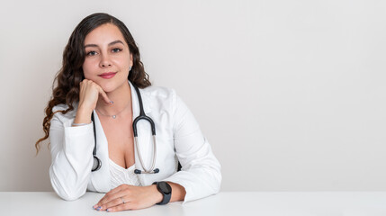Portrait of a female doctor sitting at her desk, with copy space on a white background. Beautiful medicine professional smiling looking at camera
