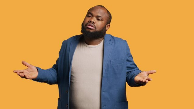 African american man shrugging shoulders, not caring, having detached apathy facial expression. Apathetic BIPOC person doing disinterest indifferent hand gesturing, studio background, camera A