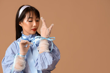 Stylish young Asian woman with blue bows on beige background