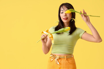 Stylish young Asian woman with bows and tulips on yellow background