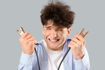 Electrocuted young man with burnt face and jumper cables on light background, closeup