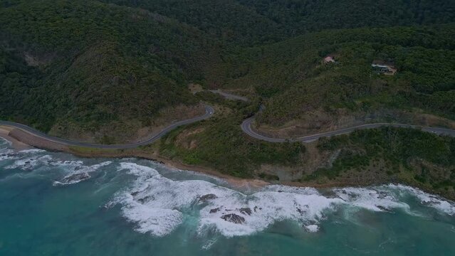 Australia's Great Ocean Road orbit drone shot showing curved highway with crashing coastal surf in Victoria