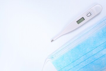 Close up Digital thermometer and blue face mask on white background, Medical supplies, protective,...