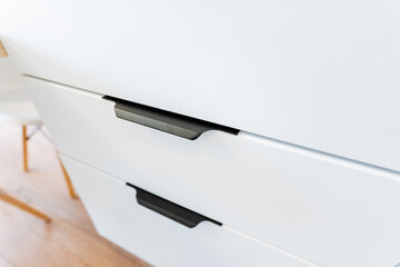 Closeup of a white wooden dresser with sleek black handles
