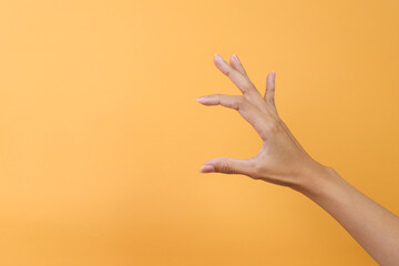 Woman hand measuring invisible items or showing small amount of something on yellow background