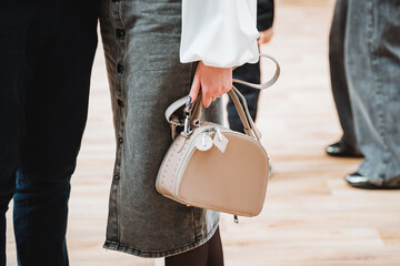 Woman holding beige purse in hand, wearing grey blazer with white sleeve
