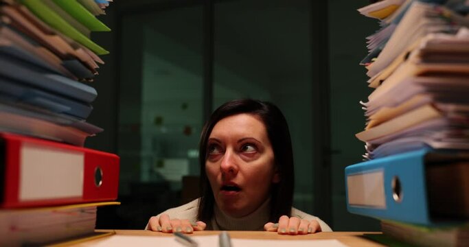 Stressed woman at work at night looking at stack of documents