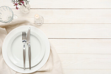 Table setting with beautiful flowers and burning candle on white wooden background
