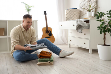 Young man folding clothes on floor at home