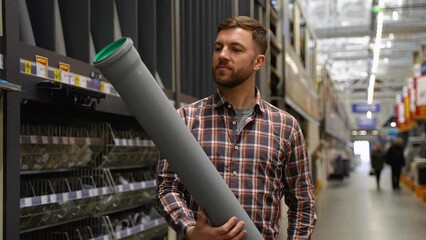 Workman choosing sewer pipes standing near the showcase of the plumbing shop