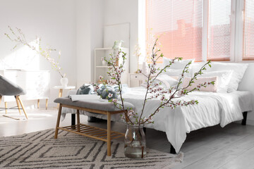 Vase with blooming branches on floor in interior of light bedroom