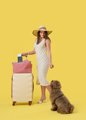 Female traveler with suitcase and cute poodle on yellow background