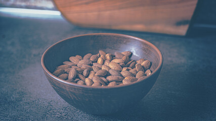 Almonds in a clay plate on the table. Blue tint.16-9