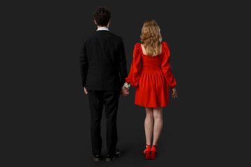 Beautiful couple dressed for prom holding hands on black background, back view