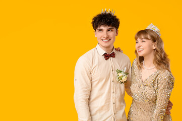 Happy prom couple in crowns on yellow background