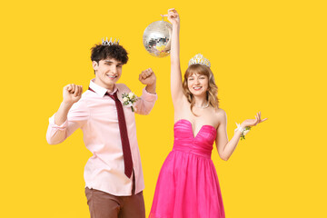 Happy prom couple in crowns with disco ball on yellow background